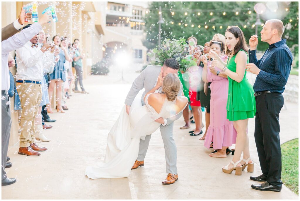 Groom dips bride for a kiss during bubble exit | Grand National Wedding | Photography by Amanda Horne