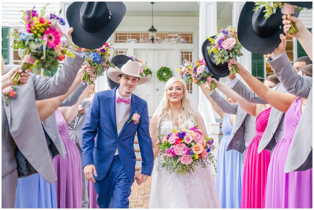 Bride and groom walk through floral tunnel with cowboy hats | Coosada Alabama Wedding Photographer Amanda Horne