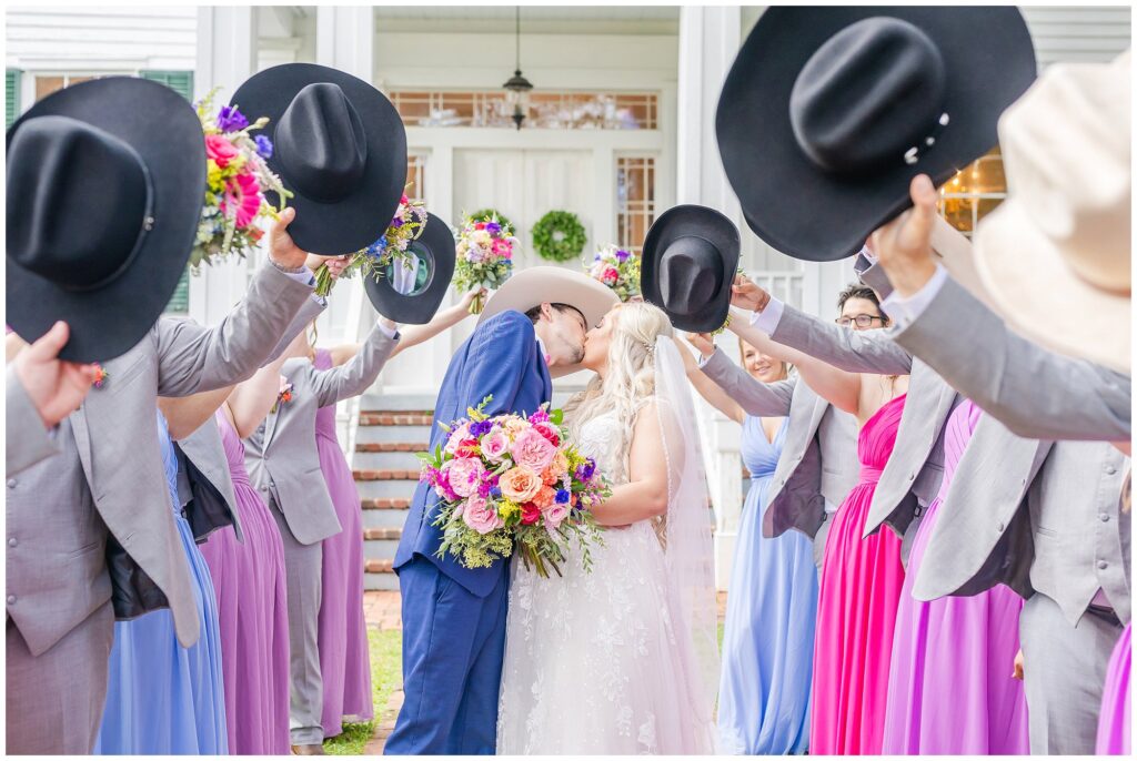 Bride and groom share a kiss surrounded by bouquets and cowboy hats | Coosada Alabama Wedding Photographer Amanda Horne