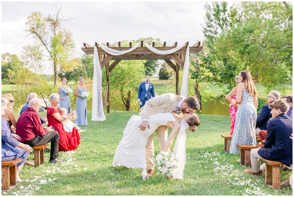 Christopher and Abigail dip kiss in aisle after Farm at Lullwater wedding ceremony
