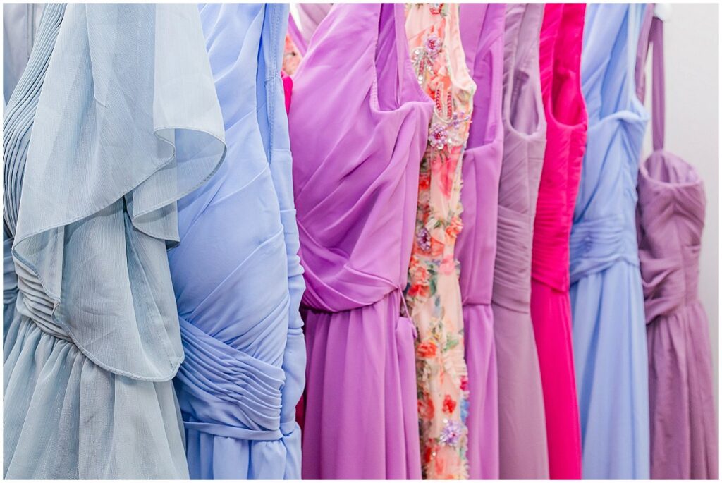 Mismatched bridesmaid dresses in shades of blue purple and pink hanging on rack, wedding trends
